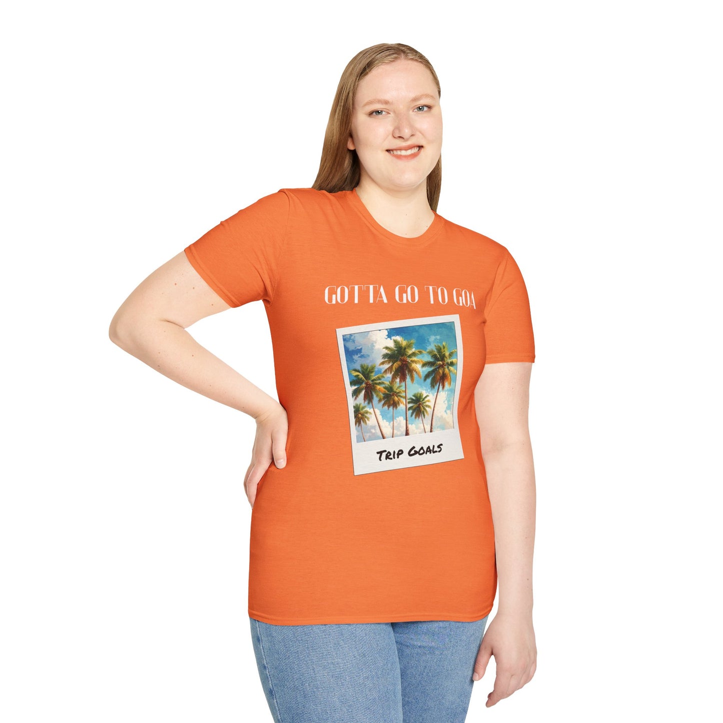 a woman wearing a heather orange shirt that says gotta go to goa with a graphic of goa beach as a postcard that says trip goals